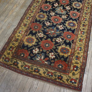 Ornate indigo rug featuring rust, gold, and blue floral motifs laid over distressed light wooden planks.