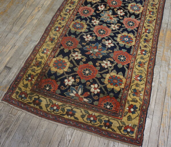 Ornate indigo rug featuring rust, gold, and blue floral motifs laid over distressed light wooden planks.