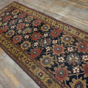 Navy runner with large red and gold floral motifs rests on worn light-colored hardwood flooring.