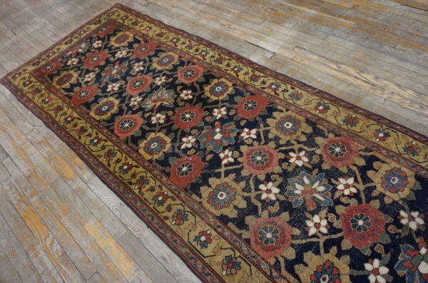 Navy runner with large red and gold floral motifs rests on worn light-colored hardwood flooring.