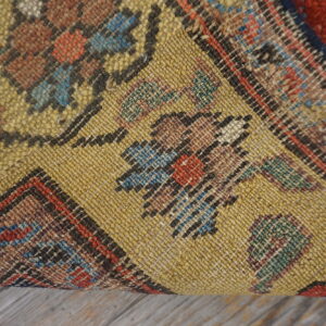 The textured yellow backing of a colorful patterned rug rests on weathered gray wood floor.