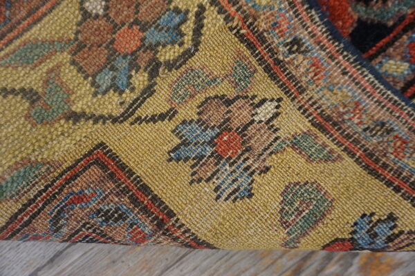 The textured yellow backing of a colorful patterned rug rests on weathered gray wood floor.