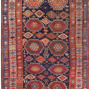 Navy blue rug with repeating red, orange, and teal geometric medallions and a complex tribal border.