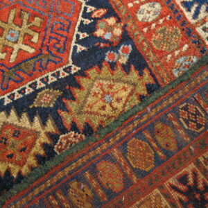 Intricate red, navy, and khaki geometric rug patterns meet a flatwoven edge, separated by a green selvage.