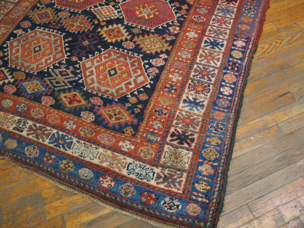 Geometric rug featuring navy field, rust border, and light accents shown on distressed hardwood floor.