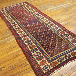 Red and blue tribal runner rug with repeating geometric patterns lies on a rustic wooden floor.
