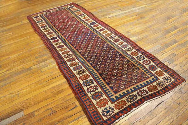 Red and blue tribal runner rug with repeating geometric patterns lies on a rustic wooden floor.