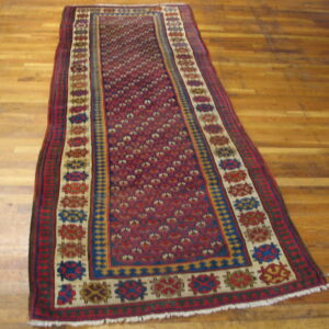 Geometric red runner with multiple colorful borders sits on worn plank hardwood flooring.