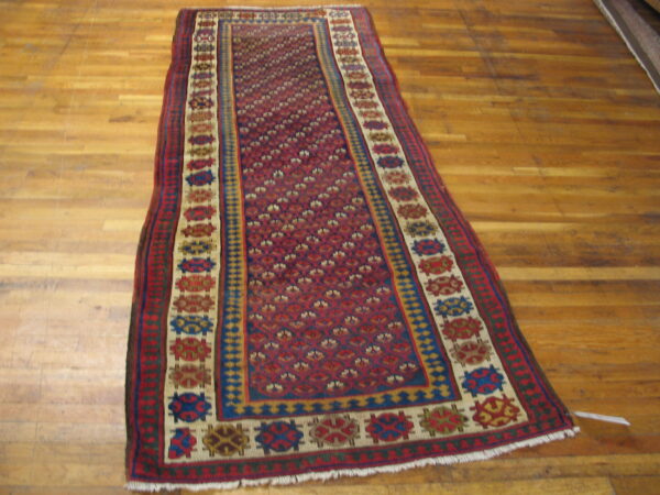 Geometric red runner with multiple colorful borders sits on worn plank hardwood flooring.