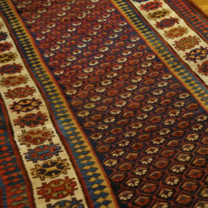 Navy and red geometric runner rug with wide, creamy borders featuring stylized medallions on wood flooring.