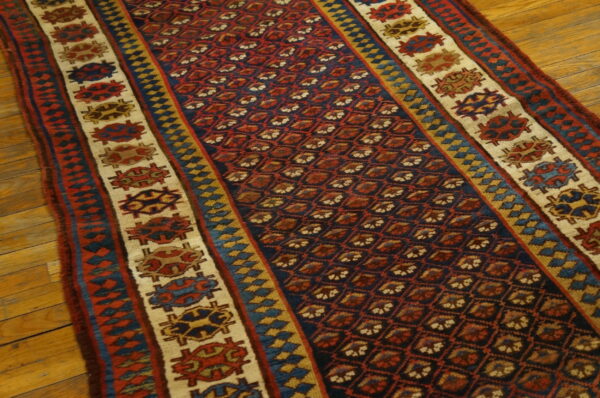 Navy and red geometric runner rug with wide, creamy borders featuring stylized medallions on wood flooring.