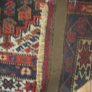 Two adjacent, dark geometric patterned rugs in red, blue, and white frame a central tan panel.