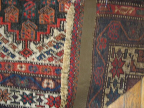 Two adjacent, dark geometric patterned rugs in red, blue, and white frame a central tan panel.