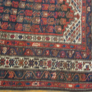 Geometric rug detail showing multiple borders in dark blue, deep red, and cream intricate patterns.