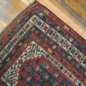Geometric patterned rug corner in deep red and blue tones contrasts with light brown wooden floorboards.