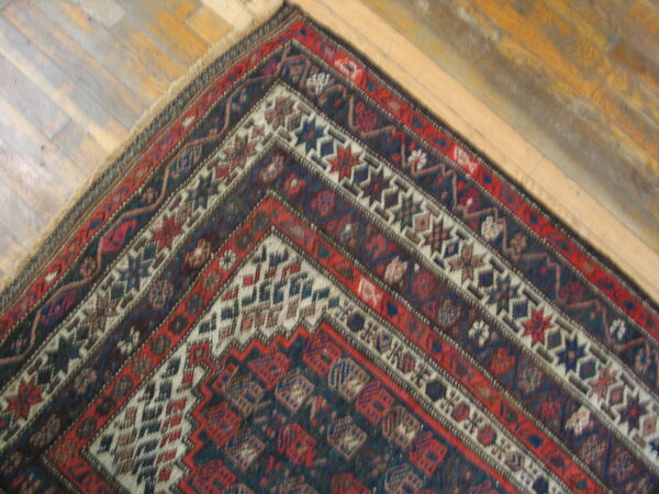 Geometric patterned rug corner in deep red and blue tones contrasts with light brown wooden floorboards.