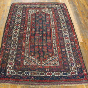 Geometric rug with deep red and navy repeating motifs and multiple borders on wood floors.