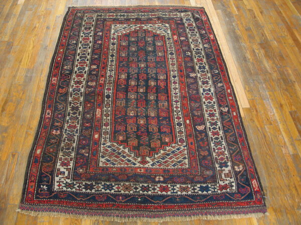 Geometric rug with deep red and navy repeating motifs and multiple borders on wood floors.