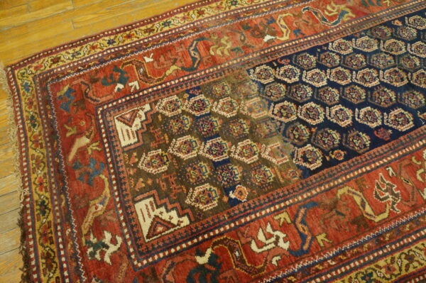 Geometric rug in shades of red, navy, brown, and gold displayed on yellow wood flooring.