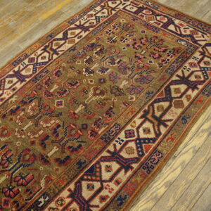 A richly patterned rug with an olive field and navy, cream, and red geometric borders rests on distressed wood planks.