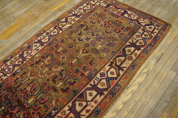 A richly patterned rug with an olive field and navy, cream, and red geometric borders rests on distressed wood planks.