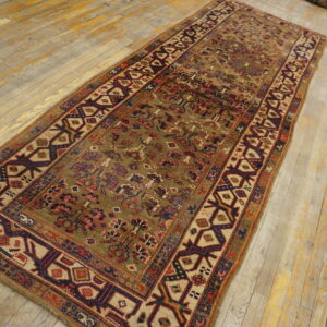Distressed runner rug with geometric patterns in red and navy rests on light, worn wood flooring.