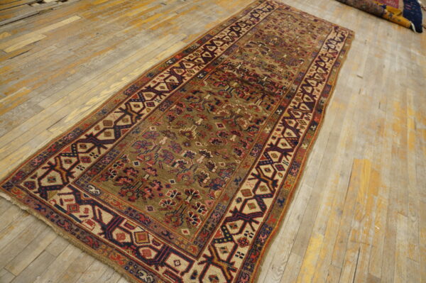 Distressed runner rug with geometric patterns in red and navy rests on light, worn wood flooring.
