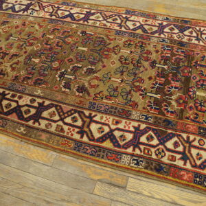 Geometric runner rug with an olive field and red and blue accents placed on light wood planks.