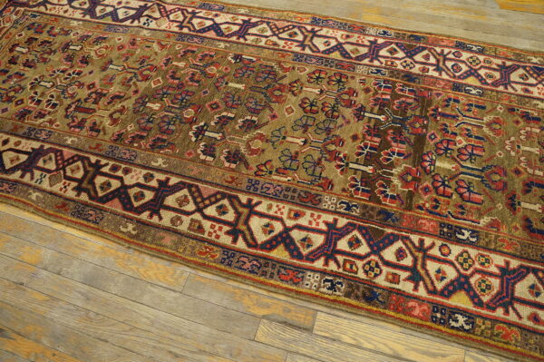 Geometric runner rug with an olive field and red and blue accents placed on light wood planks.