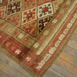 A thick pile geometric rug featuring tan, red, brown, and cream colors rests on rustic wooden floorboards.