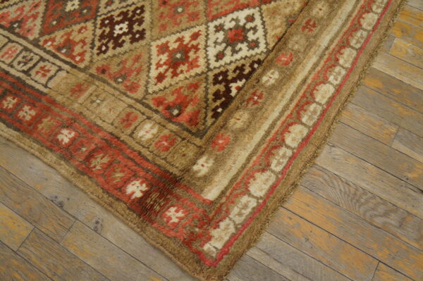 A thick pile geometric rug featuring tan, red, brown, and cream colors rests on rustic wooden floorboards.