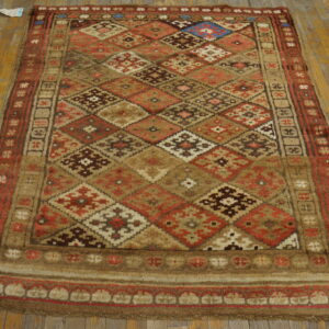 Geometric diamond rug in warm tones of brown, red, and tan resting on light wooden planks.