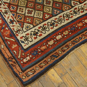 Close-up of a geometric rug corner in red, navy, and beige, resting on distressed wood planks.