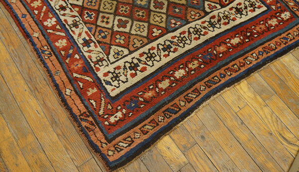 Close-up of a geometric rug corner in red, navy, and beige, resting on distressed wood planks.
