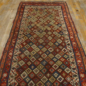 Low-pile runner rug with a dense red, blue, and beige diamond pattern resting on distressed wood floors.
