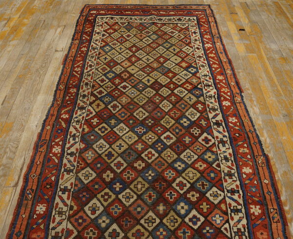 Low-pile runner rug with a dense red, blue, and beige diamond pattern resting on distressed wood floors.