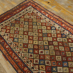 A multicolored rug with a geometric grid pattern lies on distressed yellow wood planks.