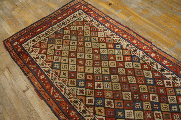 A multicolored rug with a geometric grid pattern lies on distressed yellow wood planks.