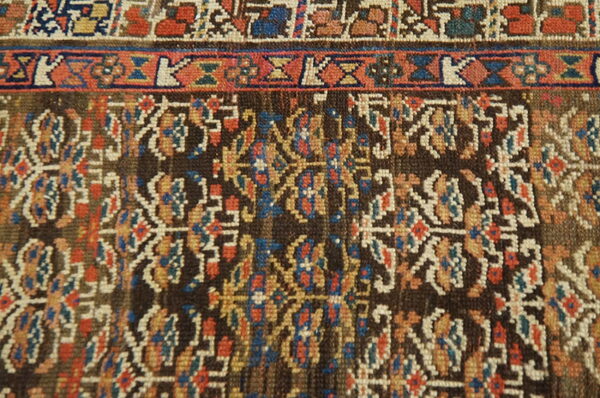 Detailed view of a rug displaying a dark brown field with colorful ornate motifs and multiple geometric borders.