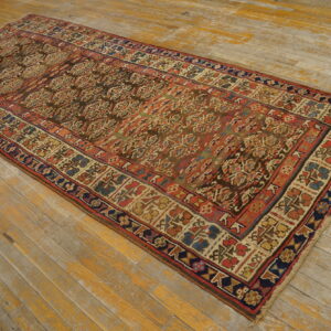 Low-pile runner rug featuring complex red, blue, and brown geometric patterns on distressed wood flooring.