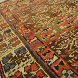 Low-pile rug detail showing borders and field with dark brown, olive, red, and blue geometric motifs.