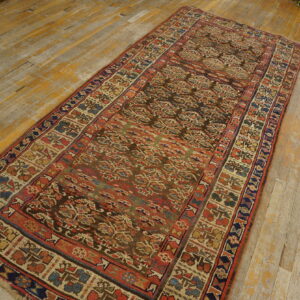 Low-pile runner with intricate patterns in brown, red, blue, and beige placed on worn plank flooring.