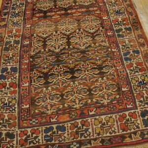 Low-pile tribal rug featuring dark brown, red, and blue geometric patterns rests on distressed yellow wood flooring.