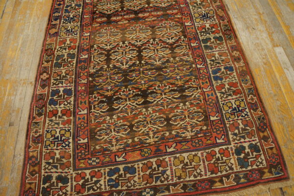 Low-pile tribal rug featuring dark brown, red, and blue geometric patterns rests on distressed yellow wood flooring.