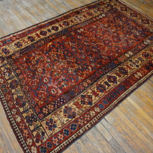 Rust and navy patterned area rug with beige borders displayed on worn wood plank flooring.
