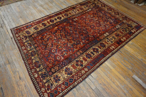 Rust and navy patterned area rug with beige borders displayed on worn wood plank flooring.