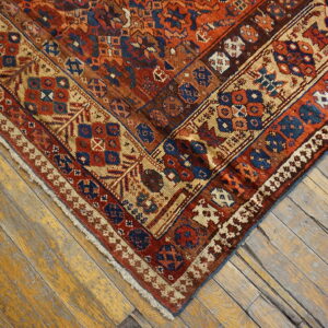 Intricate geometric rug in rust, blue, and tan against distressed, wide plank wood floorboards.