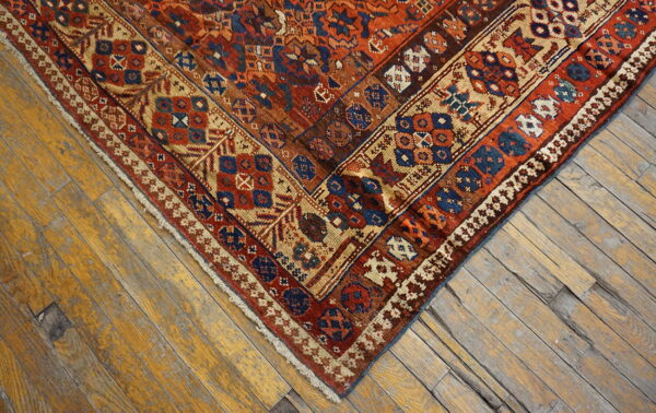 Intricate geometric rug in rust, blue, and tan against distressed, wide plank wood floorboards.