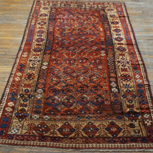 Deep red rug with complex navy and tan geometric motifs on light wooden plank flooring.