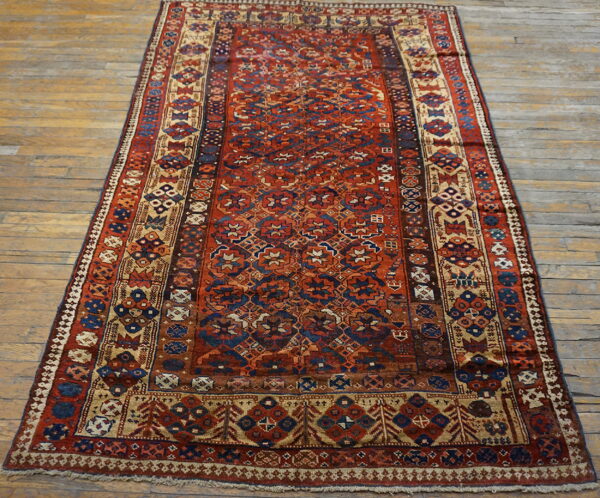 Deep red rug with complex navy and tan geometric motifs on light wooden plank flooring.